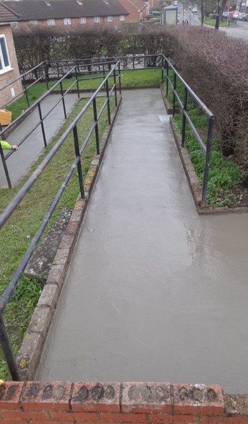 Freshly laid concrete ramp between metal handrails